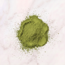 A small mound of bright green powder, likely matcha or tea powder, scattered on a white marble surface.